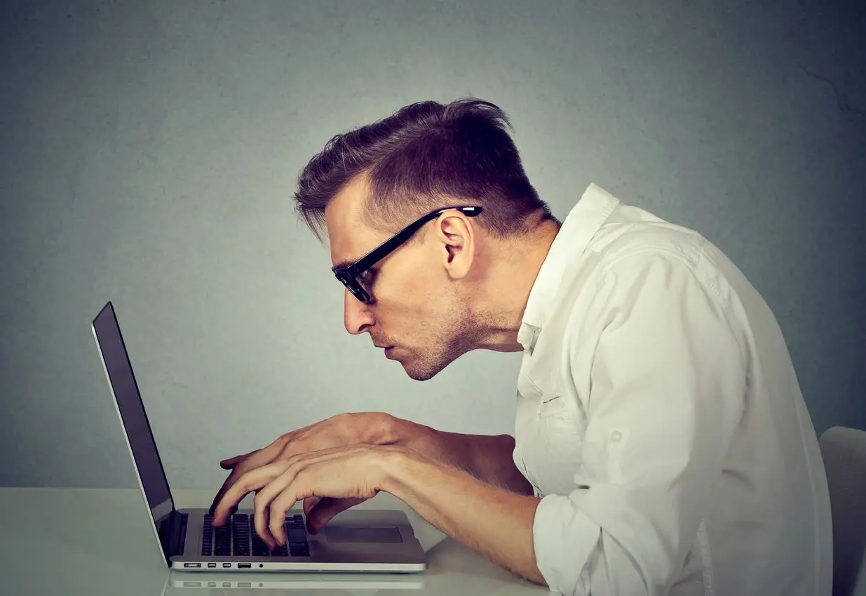 A man with glasses is typing on his laptop.